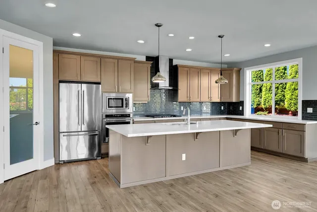 a large kitchen with stainless steel appliances granite countertop a refrigerator a sink dishwasher a stove and a refrigerator with wooden floor