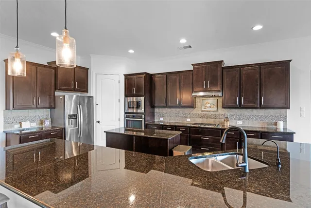 a kitchen with stainless steel appliances granite countertop a stove top oven a sink a refrigerator a stove a dining table and chairs