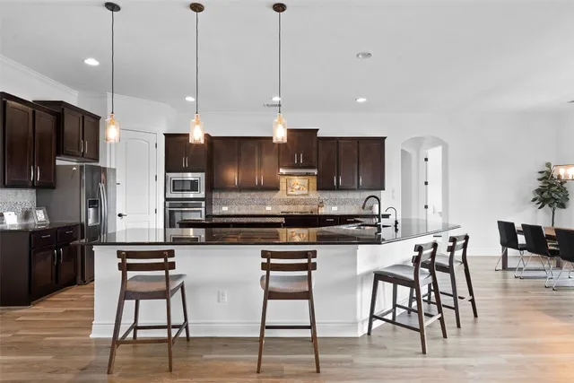 a kitchen with stainless steel appliances kitchen island granite countertop a stove a refrigerator a kitchen island a dining table and chairs with wooden floors