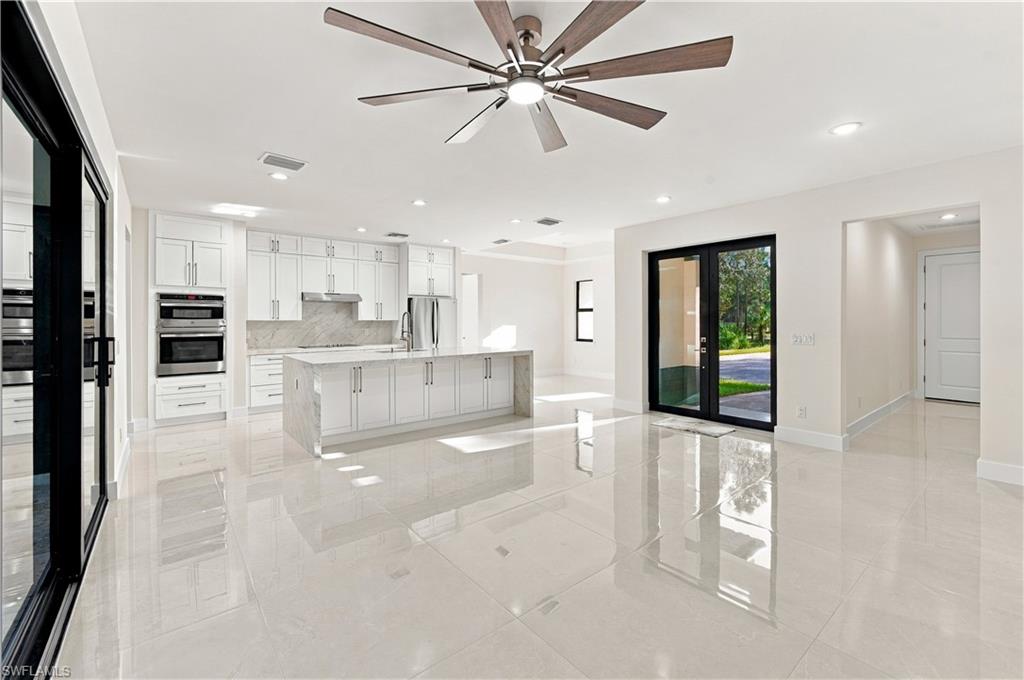 Spacious open-concept living area featuring large format light-toned tile flooring, a contemporary ceiling fan, recessed lighting, and a kitchen island with integrated sink