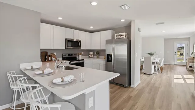 a kitchen with stainless steel appliances granite countertop a refrigerator a microwave a stove a sink a dining table and chairs with wooden floor