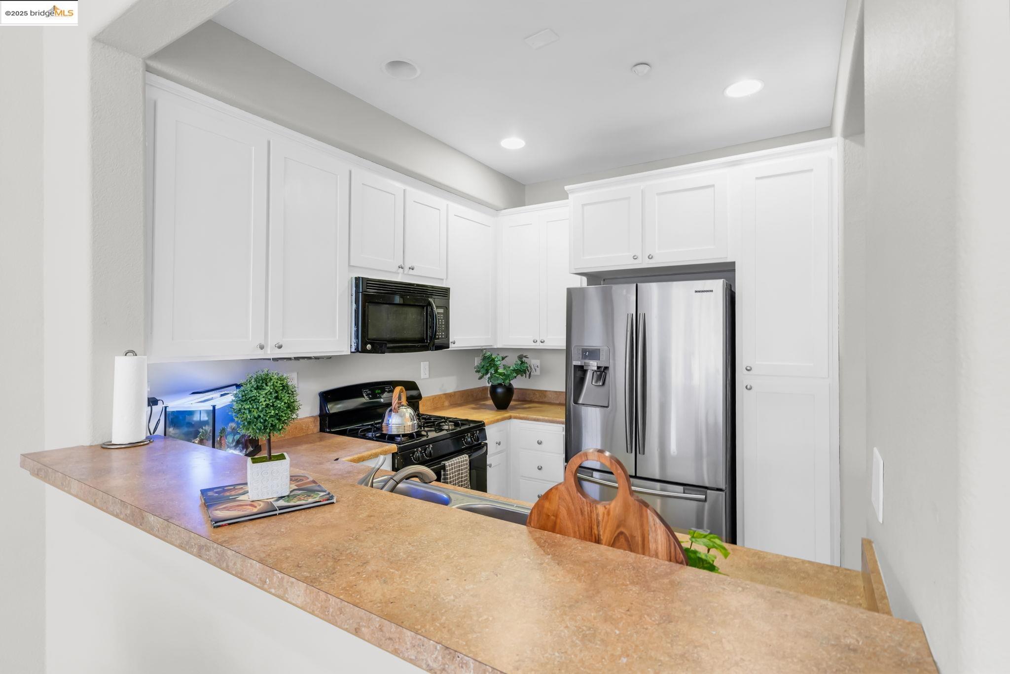 6063 Old Quarry Loop Oakland, CA 94605 - Photo 11 of 36 a kitchen with stainless steel appliances granite countertop a refrigerator a stove a microwave a sink dishwasher and white cabinets with wooden floor