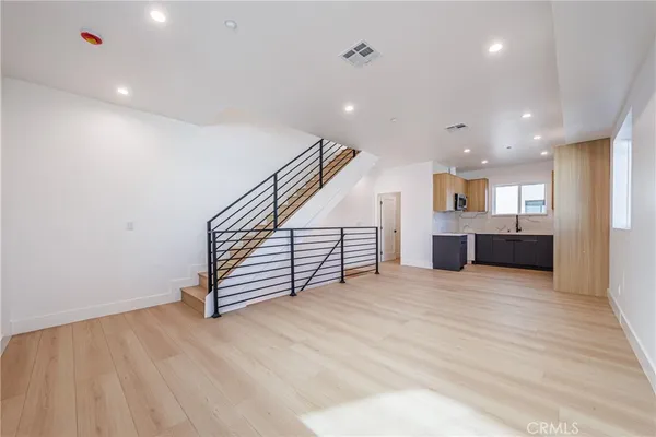 a view of an empty room with wooden floor and a kitchen