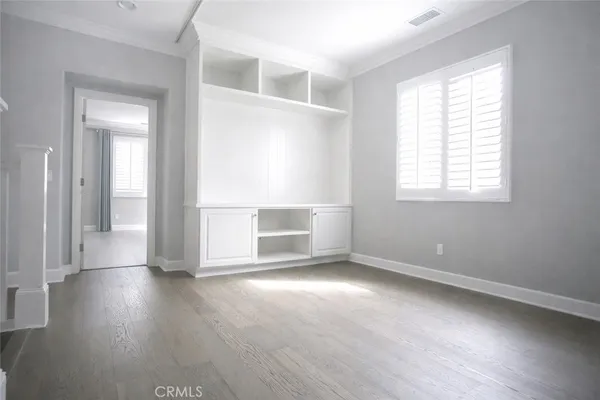 an empty room with wooden floor cabinet and windows