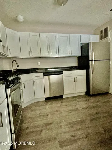 a kitchen with granite countertop a refrigerator a sink and white cabinets