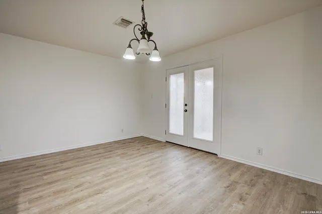 a view of an empty room with wooden floor and chandelier