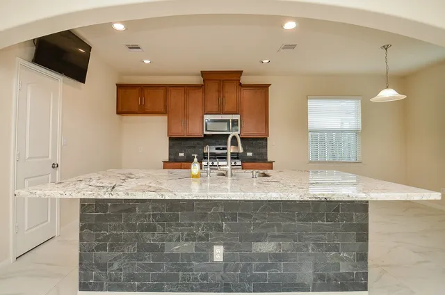 a kitchen with kitchen island granite countertop a sink a counter top space cabinets and stainless steel appliances