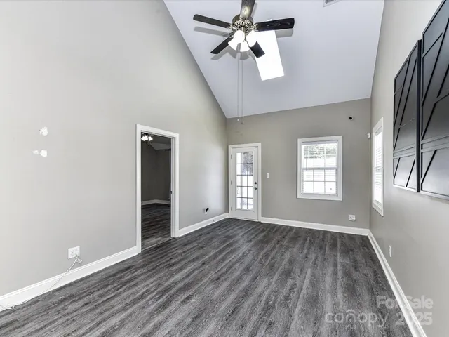 an empty room with wooden floor chandelier fan and windows