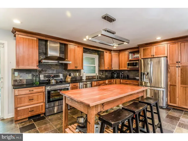 a room with stainless steel appliances kitchen island granite countertop a stove top oven a sink and a refrigerator