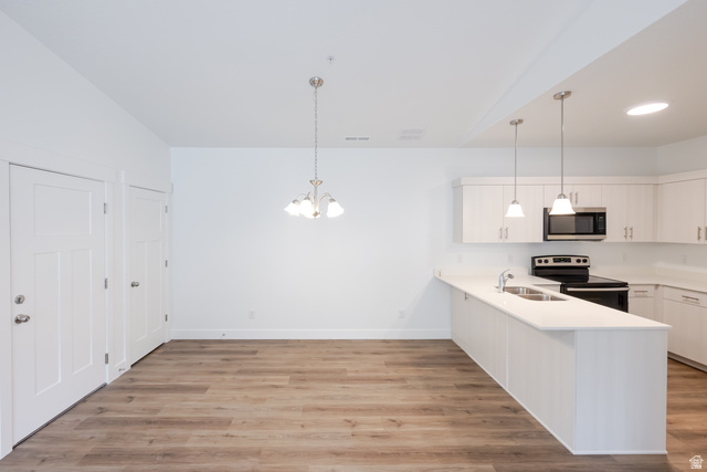 4664 South 680th West, Unit S303 Mapleton, UT 84664 - Photo 15 of 18 Open-concept living space with wood-finish flooring, a contemporary chandelier, and a kitchen featuring white cabinetry, light-colored countertops, and stainless steel appliances including a microwave and range