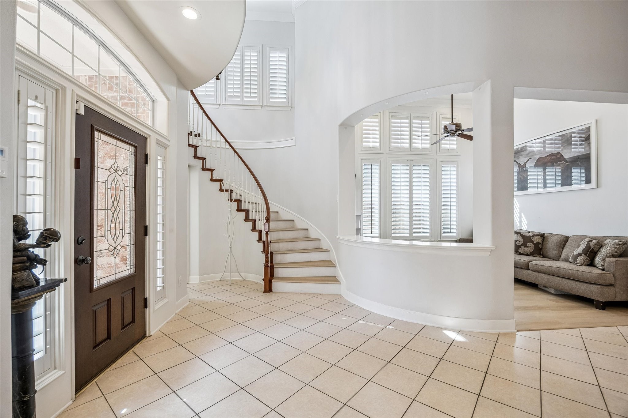 3047 Bonnebridge Way Boulevard Houston, TX 77082 - Photo 12 of 50 The inviting foyer showcases the home’s thoughtfully crafted architecture and timeless design. A stunning dark wood front door with elegant leaded glass, matching sidelights with plantation shutters, and transom windows create a grand first impression. Abundant natural light pours through multiple plantation-shuttered windows, while the clean, neutral palette enhances the home's spacious layout, creating an open, airy atmosphere that reflects understated luxury.