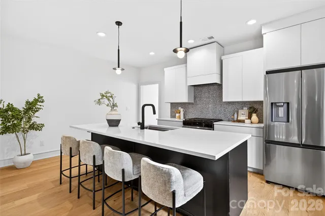 a kitchen with stainless steel appliances granite countertop a sink a refrigerator a stove a dining table and chairs with wooden floor