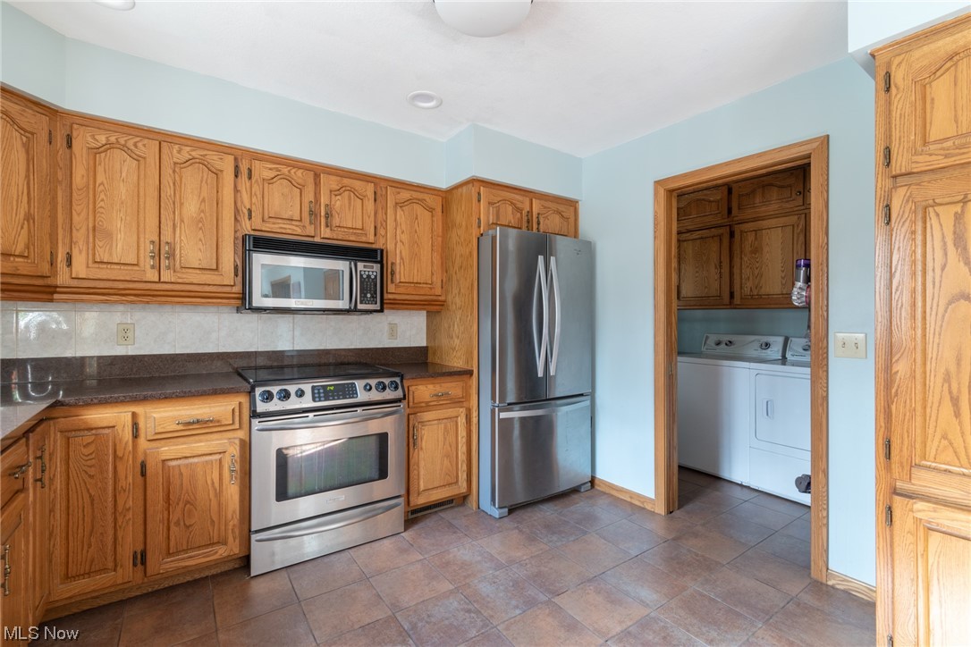 8089 Thomas Road Lisbon, OH 44432 - Photo 19 of 46 Kitchen featuring appliances with stainless steel finishes, washing machine and dryer, backsplash, and dark tile floors