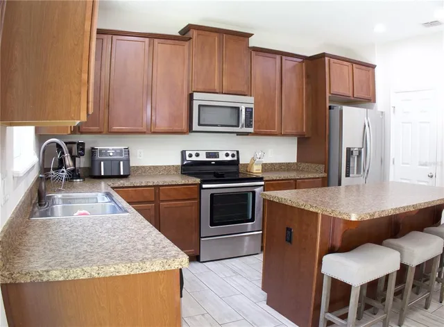 a kitchen with granite countertop kitchen island stainless steel appliances a stove a sink a microwave a refrigerator and cabinets