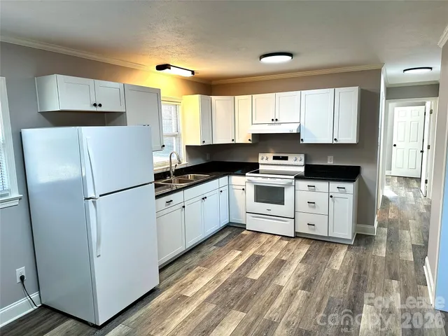 a kitchen with granite countertop a refrigerator a sink and white cabinets