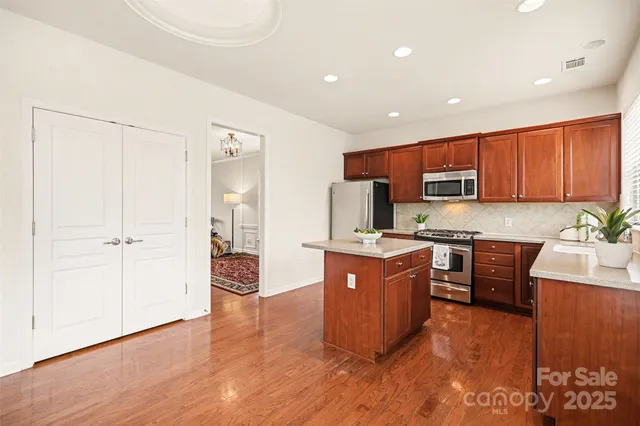 a kitchen with stainless steel appliances granite countertop a refrigerator a stove top oven and a sink with wooden floor