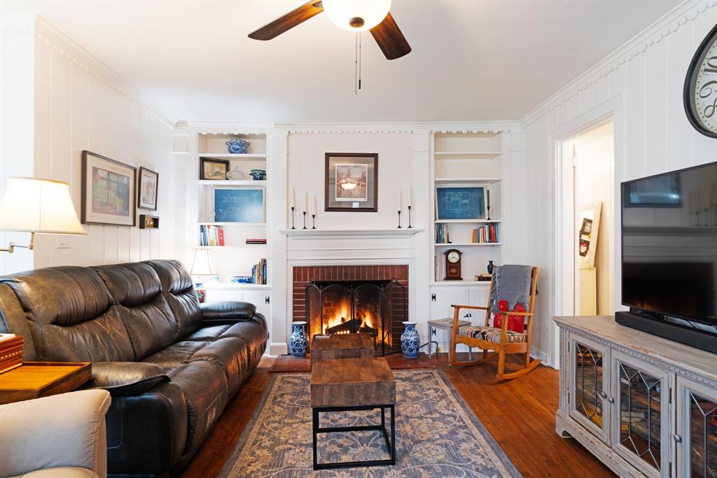Living area featuring built in shelves, ornamental molding, dark wood finished floors, ceiling fan, and a brick fireplace