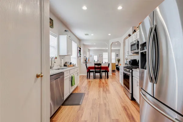 a kitchen with stainless steel appliances a refrigerator a sink dishwasher a stove and white cabinets with wooden floor