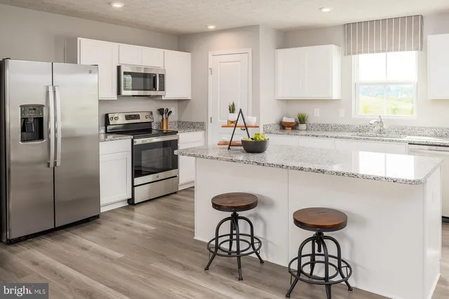 a kitchen with stainless steel appliances granite countertop a sink a stove a refrigerator cabinets and a dining table with wooden floor