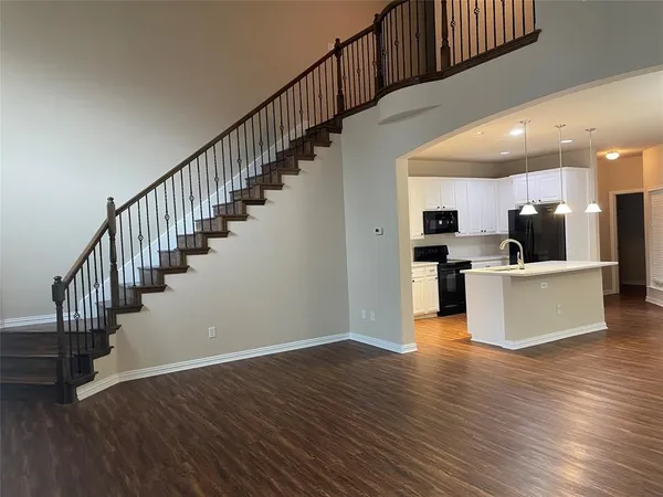 a view of a kitchen with stainless steel appliances kitchen island wooden floors granite top and a rug