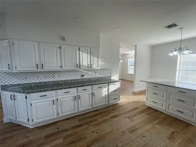 a kitchen with granite countertop a sink white cabinets and wooden floors