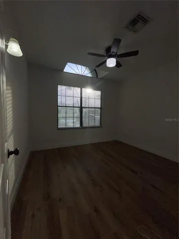 an empty room with wooden floor fan and windows