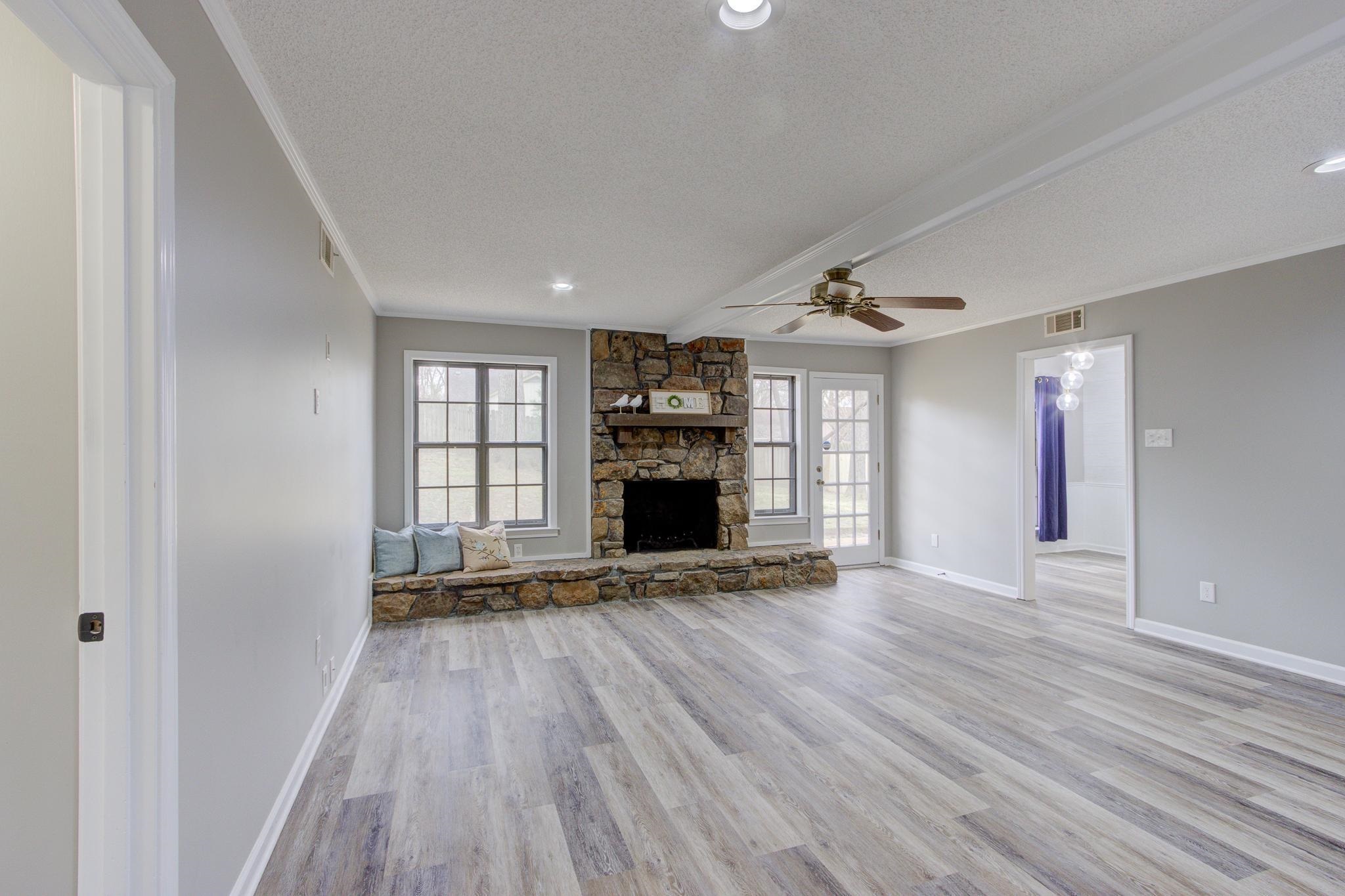 5991 Explorer Road Bartlett, TN 38134 - Photo 21 of 39 Unfurnished living room featuring wood burning fireplace, a ceiling fan, LVP floors, crown molding and door to backyard.
