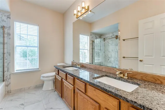 a bathroom with a granite countertop double vanity sink a mirror and a toilet