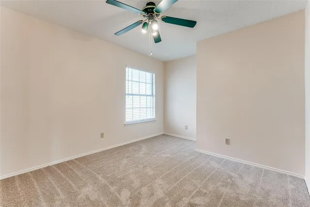 an empty room with chandelier fan and windows