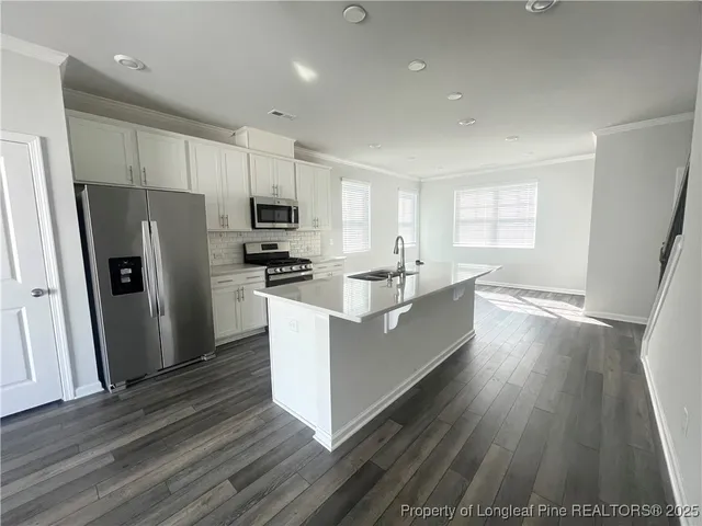 a large kitchen with stainless steel appliances a refrigerator a sink dishwasher a stove and white countertops with wooden floor