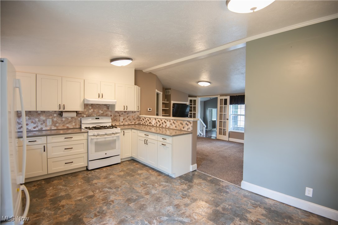 4594 Center Road Andover, OH 44003 - Photo 7 of 39 Kitchen featuring white appliances, a peninsula, tasteful backsplash, white cabinets, and dark colored carpet
