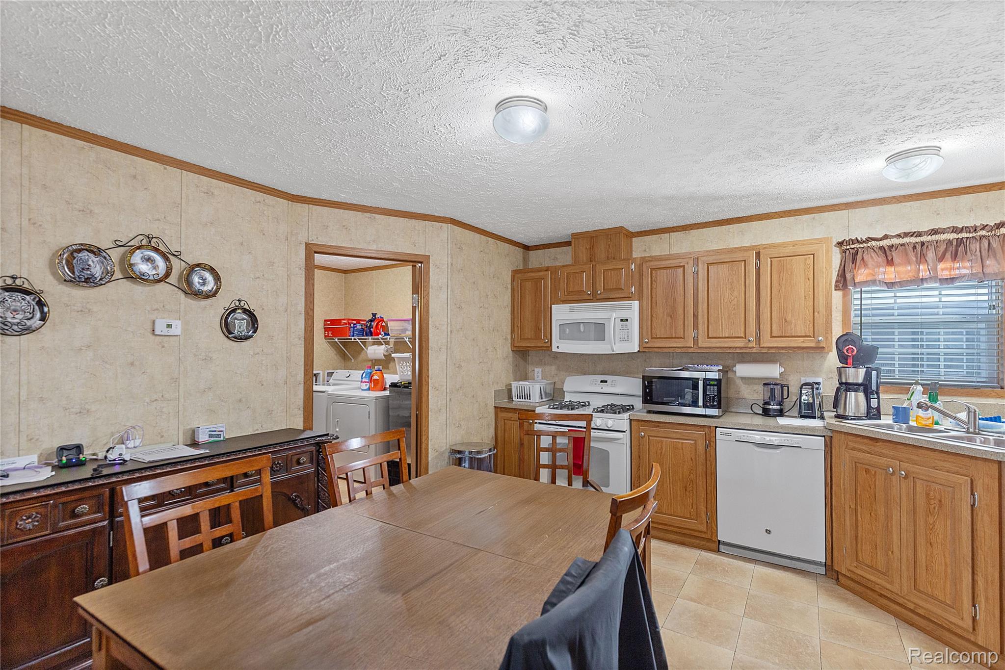 Kitchen with white appliances, light countertops, crown molding, washer and dryer, and a textured ceiling