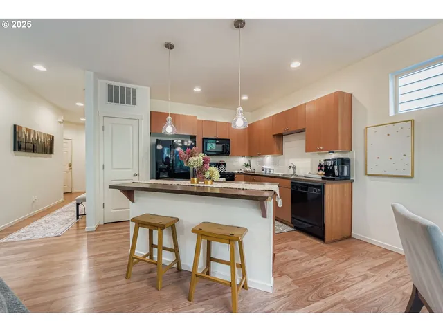a kitchen with stainless steel appliances kitchen island granite countertop a refrigerator a stove a sink dishwasher with a dining table and chairs with wooden floor