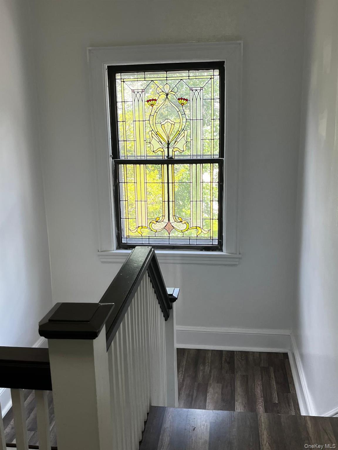 440 Mile Square Road Yonkers, NY 10701 - Photo 25 of 29 Staircase landing featuring a decorative stained glass window, dark wood-finish flooring, white painted walls, and a white and dark-stained wood balustrade