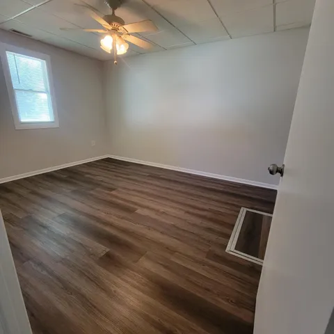 an empty room with wooden floor fan and windows