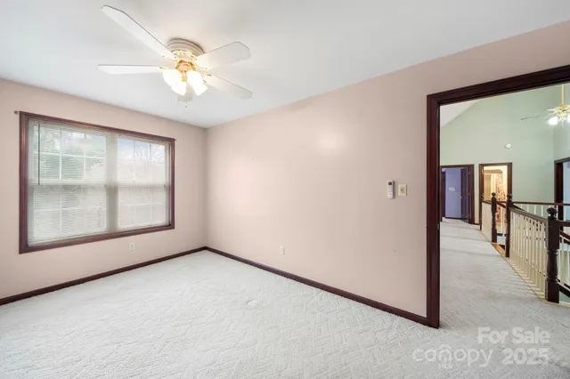 an empty room with chandelier fan and windows