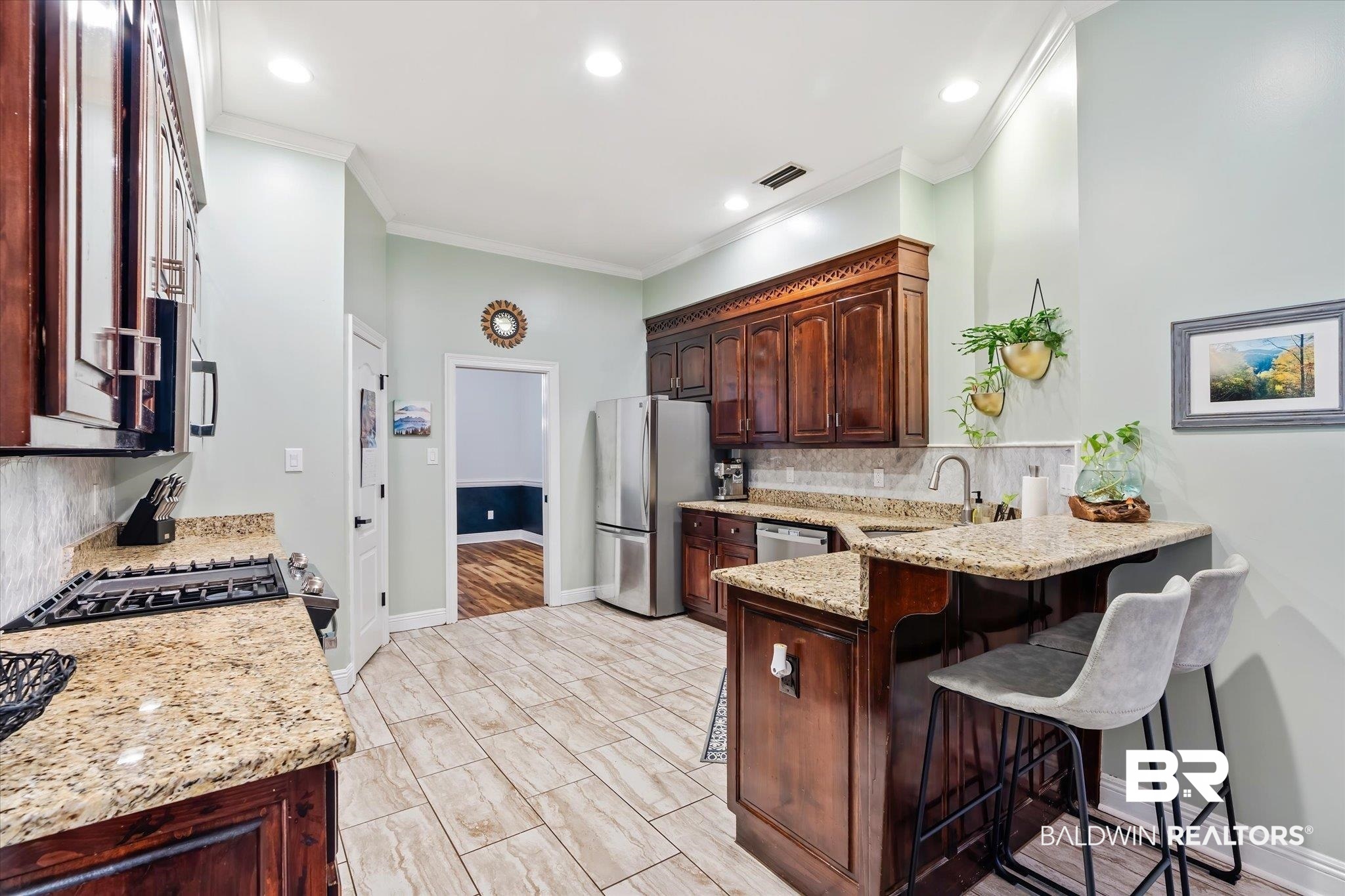 3600 Russells Lane Mobile, AL 36619 - Photo 9 of 43 Kitchen with light stone countertops, stainless steel appliances, kitchen peninsula, a kitchen bar, and ornamental molding