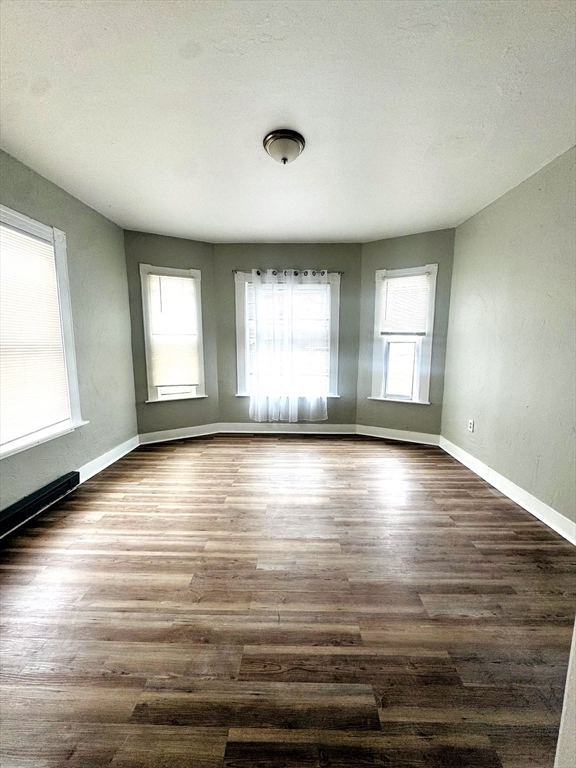 738 Central Street, Unit 2 Lowell, MA 01852 - Photo 3 of 11 an empty room with wooden floor and windows with curtains