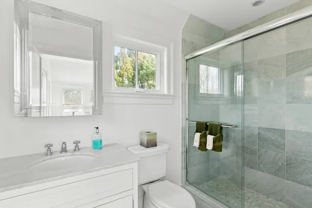 a bathroom with a granite countertop sink a toilet a mirror and shower