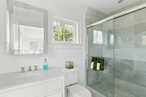 a bathroom with a granite countertop sink a toilet a mirror and shower