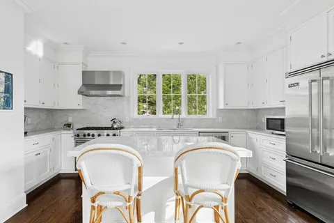 a kitchen with stainless steel appliances sink a stove a refrigerator cabinets and a dining table with wooden floor