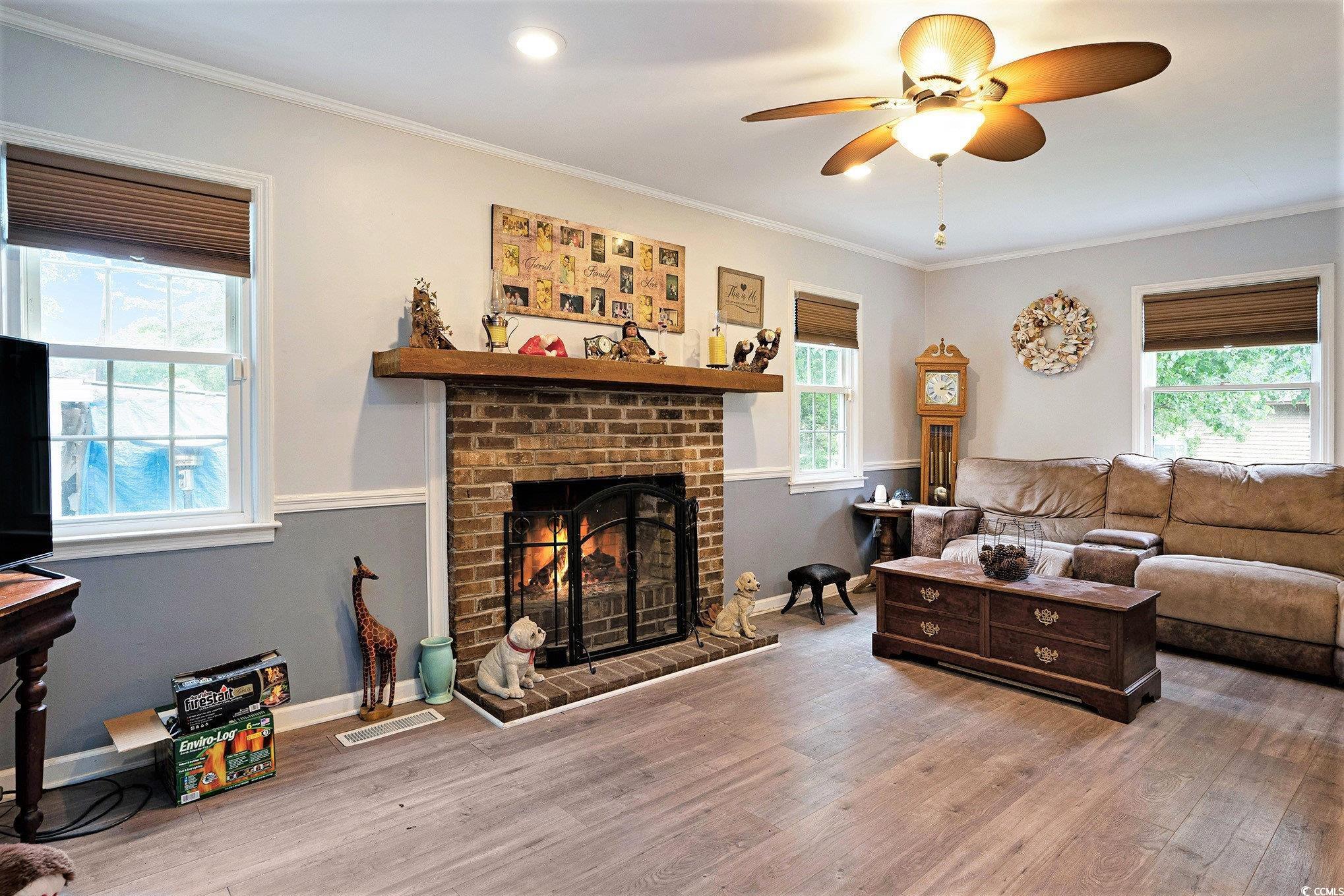Living room featuring wood finished floors, ceiling fan, a fireplace, crown molding, and baseboards