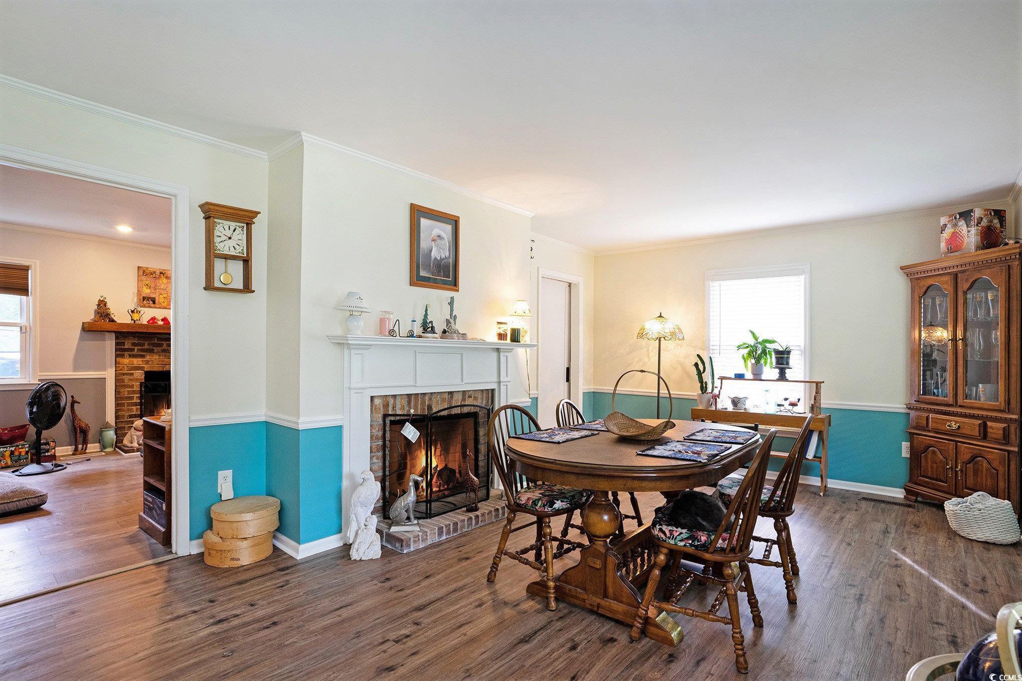 Dining space with a brick fireplace, plenty of natural light, wood finished floors, and ornamental molding