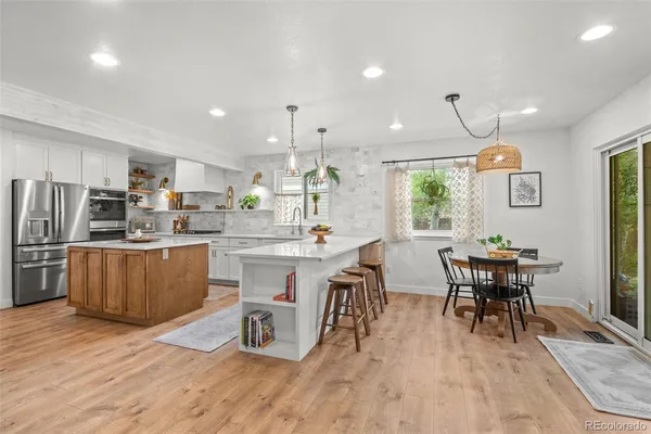 a kitchen with stainless steel appliances granite countertop a dining table chairs refrigerator and sink