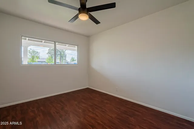 an empty room with wooden floor ceiling fan and windows