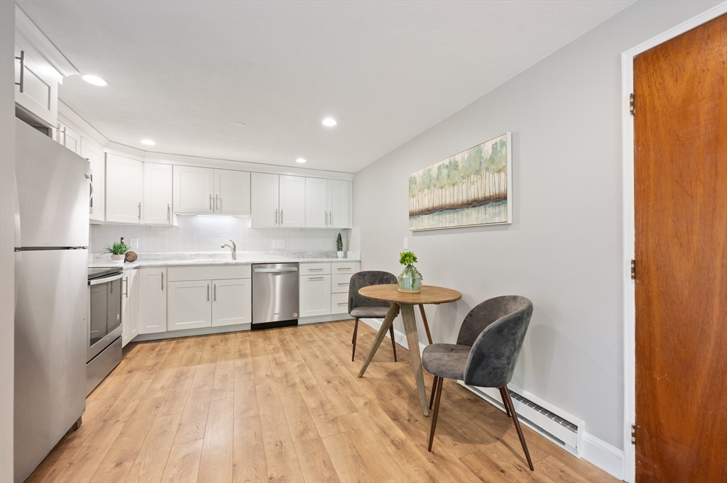 7 Walker Road, Unit 12 North Andover, MA 01845 - Photo 10 of 20 a kitchen with stainless steel appliances a white stove top oven a refrigerator a dining table and chairs with wooden floor