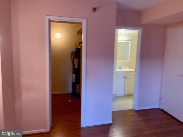 a view of an empty room with wooden floor and a bedroom