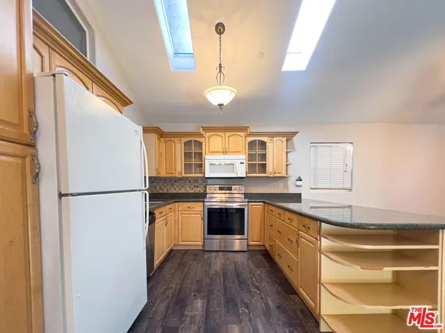 a kitchen with stainless steel appliances granite countertop a refrigerator a sink dishwasher a stove and white countertops with wooden floor