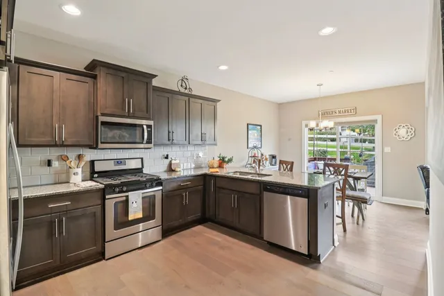 a kitchen with stainless steel appliances granite countertop a stove top oven a sink dishwasher a dining table and chairs with wooden floor