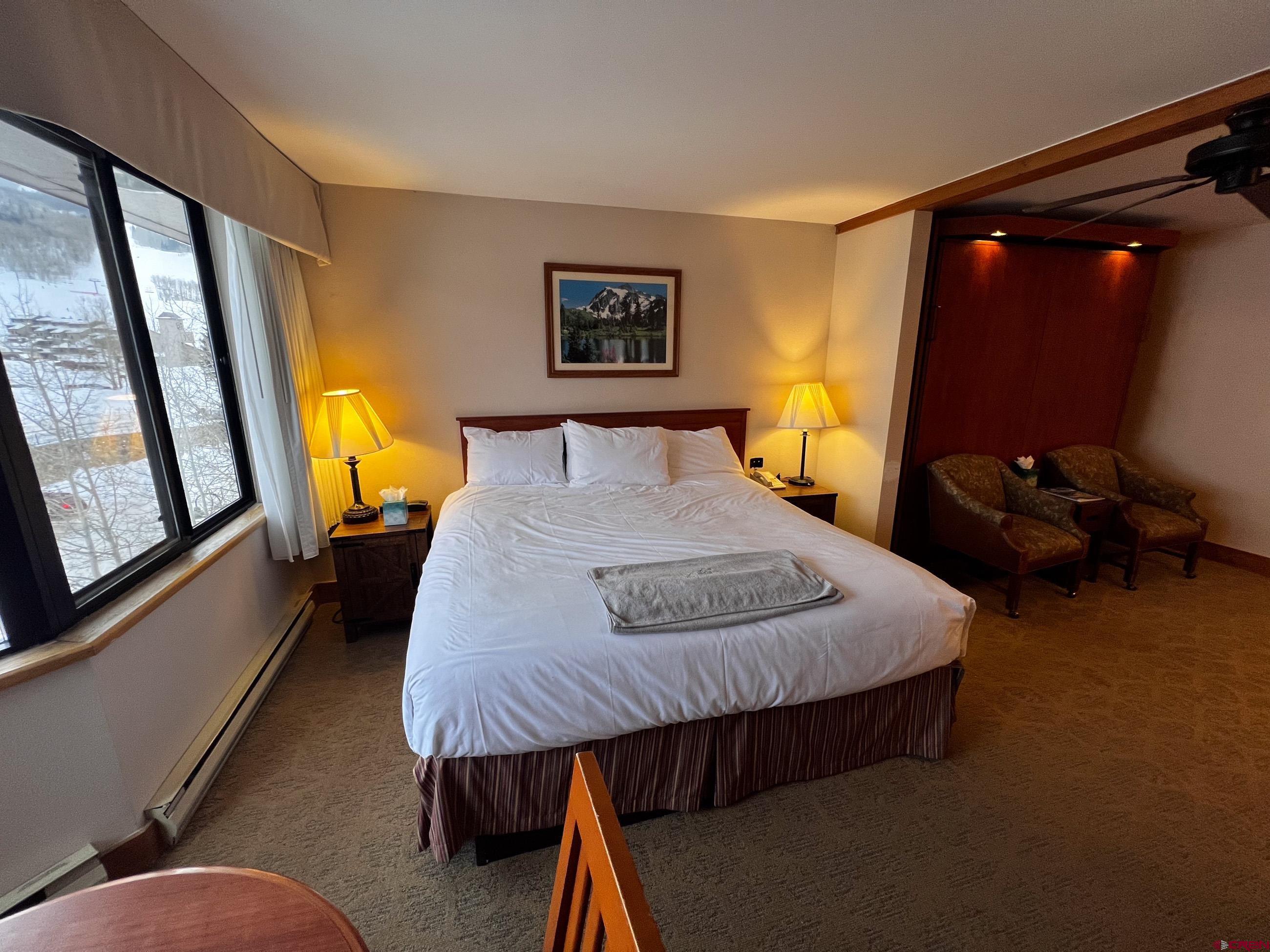 a bedroom with a bed a mirror on dresser and a large window